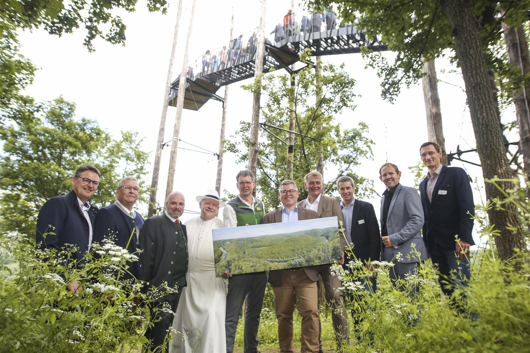 Ehrengäste wie Kräuterpfarrer Benedikt, Landesrat Ludwig Schleritzko stehen unter der Warte mit dem Bild "Blick von der Aussichtswarte".